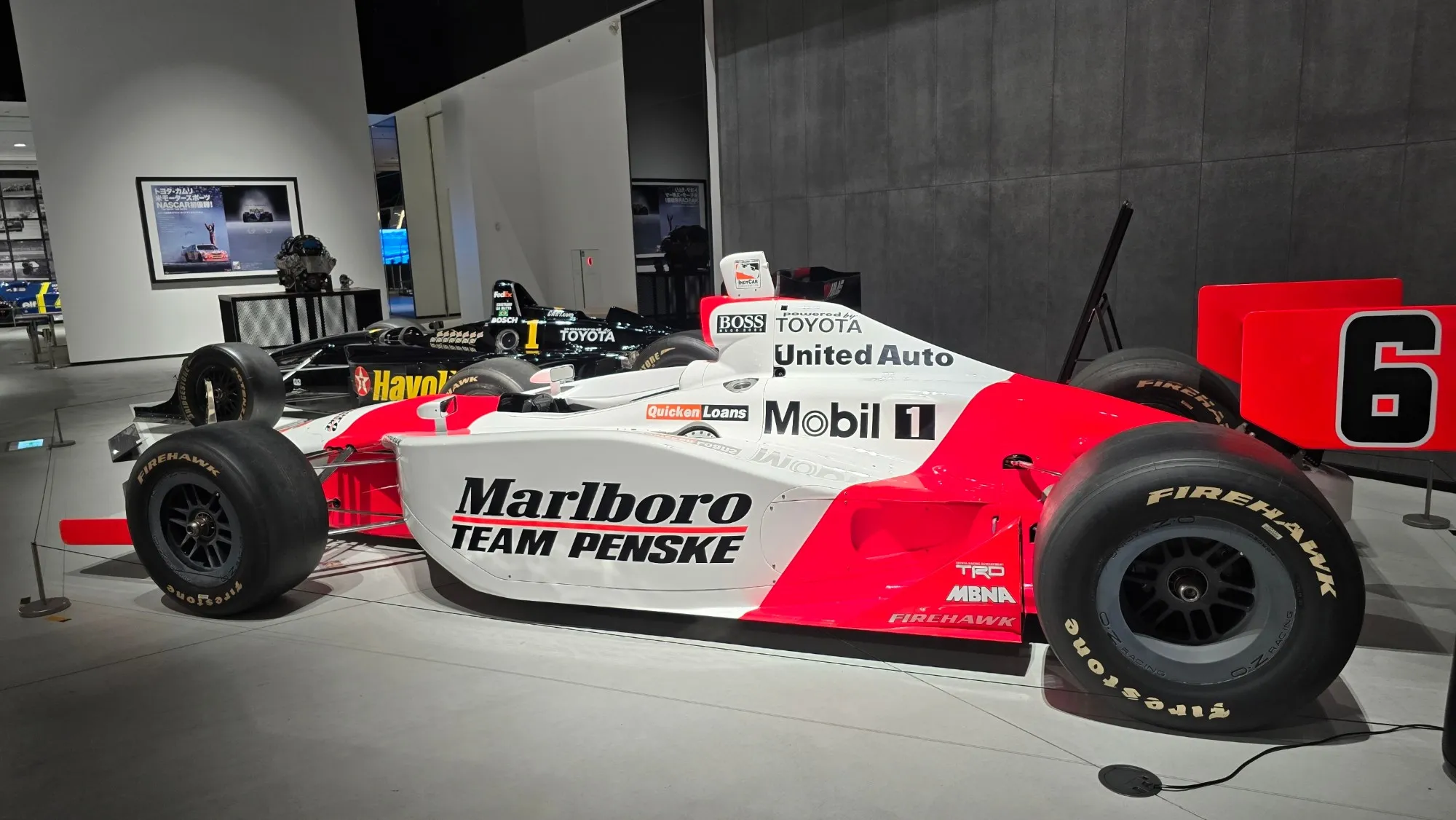 Monoplace IndyCar Toyota aux couleurs Marlboro Team Penske, exposée à côté d'une autre IndyCar Toyota noire