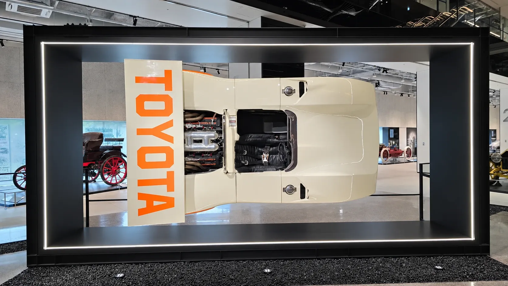 Vue plongeante sur un prototype de course Toyota crème, depuis un étage supérieur du musée