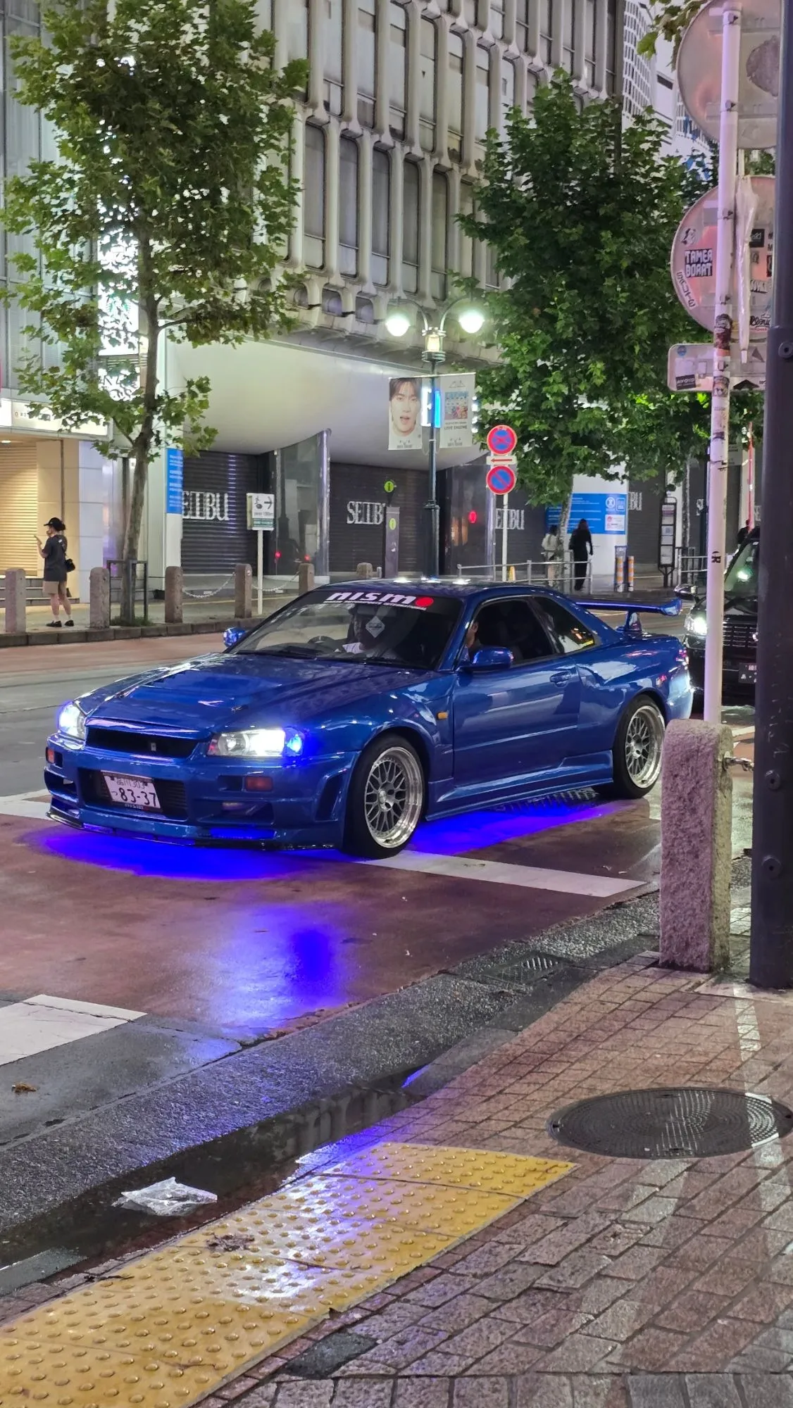 Nissan Skyline R34 bleue, phares allumés, dans une rue de Tokyo la nuit
