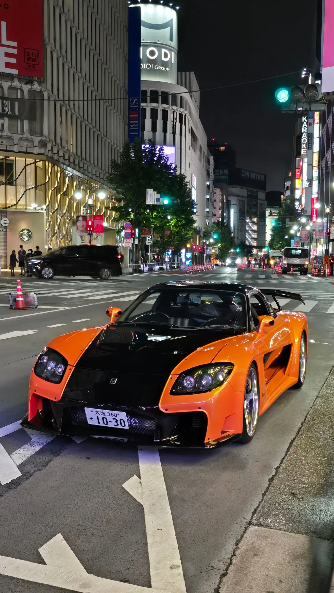 Mazda RX-7 FD Veilside orange et noire dans une rue de Tokyo la nuit