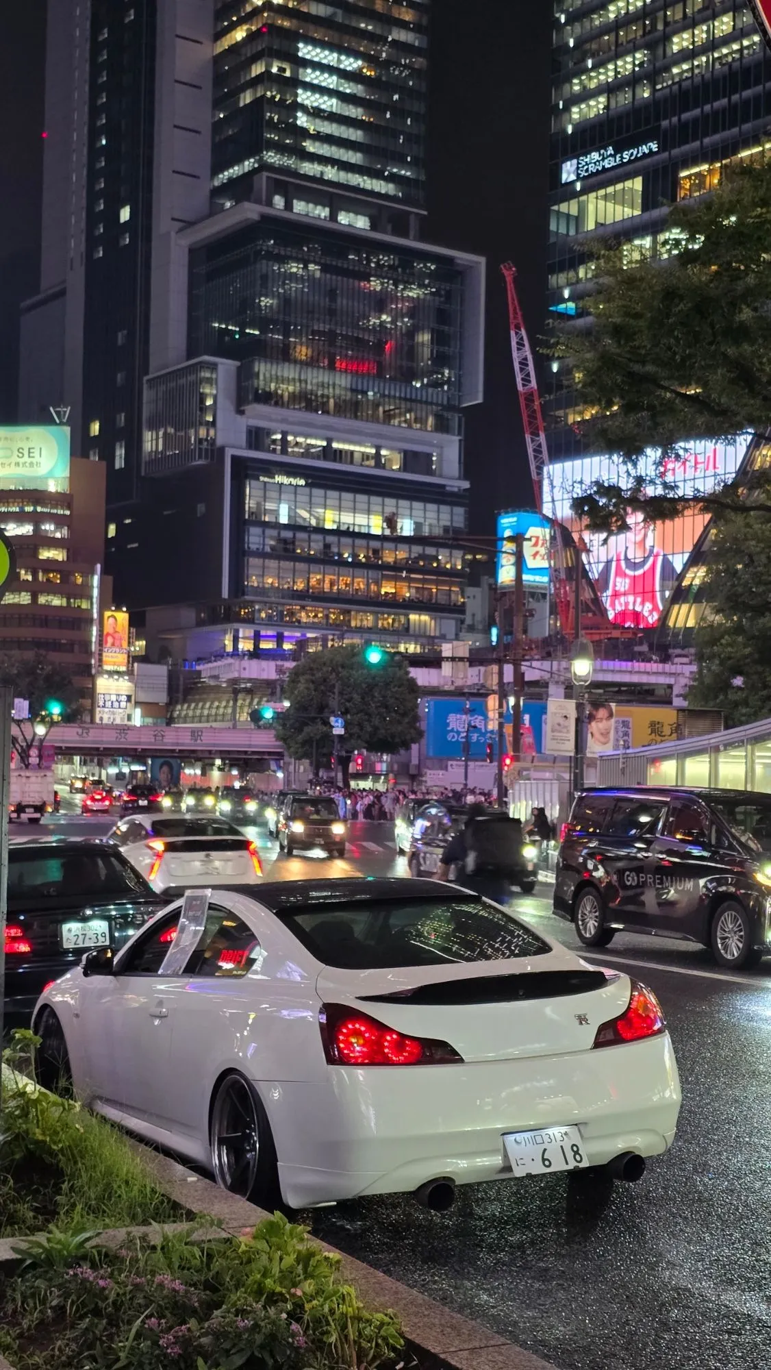 Nissan Skyline coupé blanc stancé dans le trafic de nuit à Shibuya